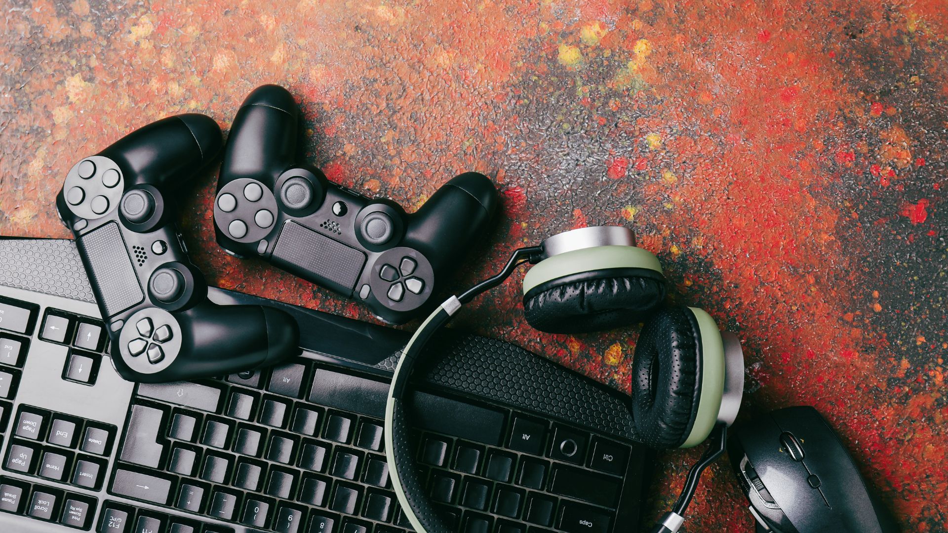 Konsola do gier, pad, słuchawki i klawiatura leżą na biurku.