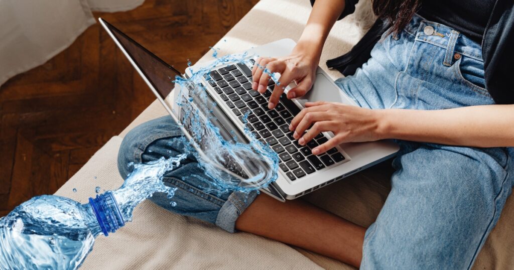 Kobieta pracuje na laptopie, w tle przewrócona butelka z wodą rozlewa się na klawiaturę
